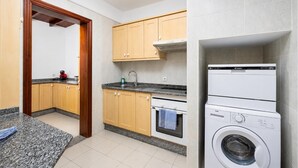Ett kompakt kök med träskåp, en inbyggd ugn, en tvättmaskin och en liten arbetsbänk.