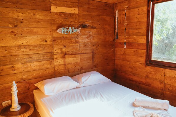 Une chambre aménagée dans une cabane en bois, avec un lit, une décoration sur le thème d’un phare et un panneau indiquant « PLAGE » sur le mur.