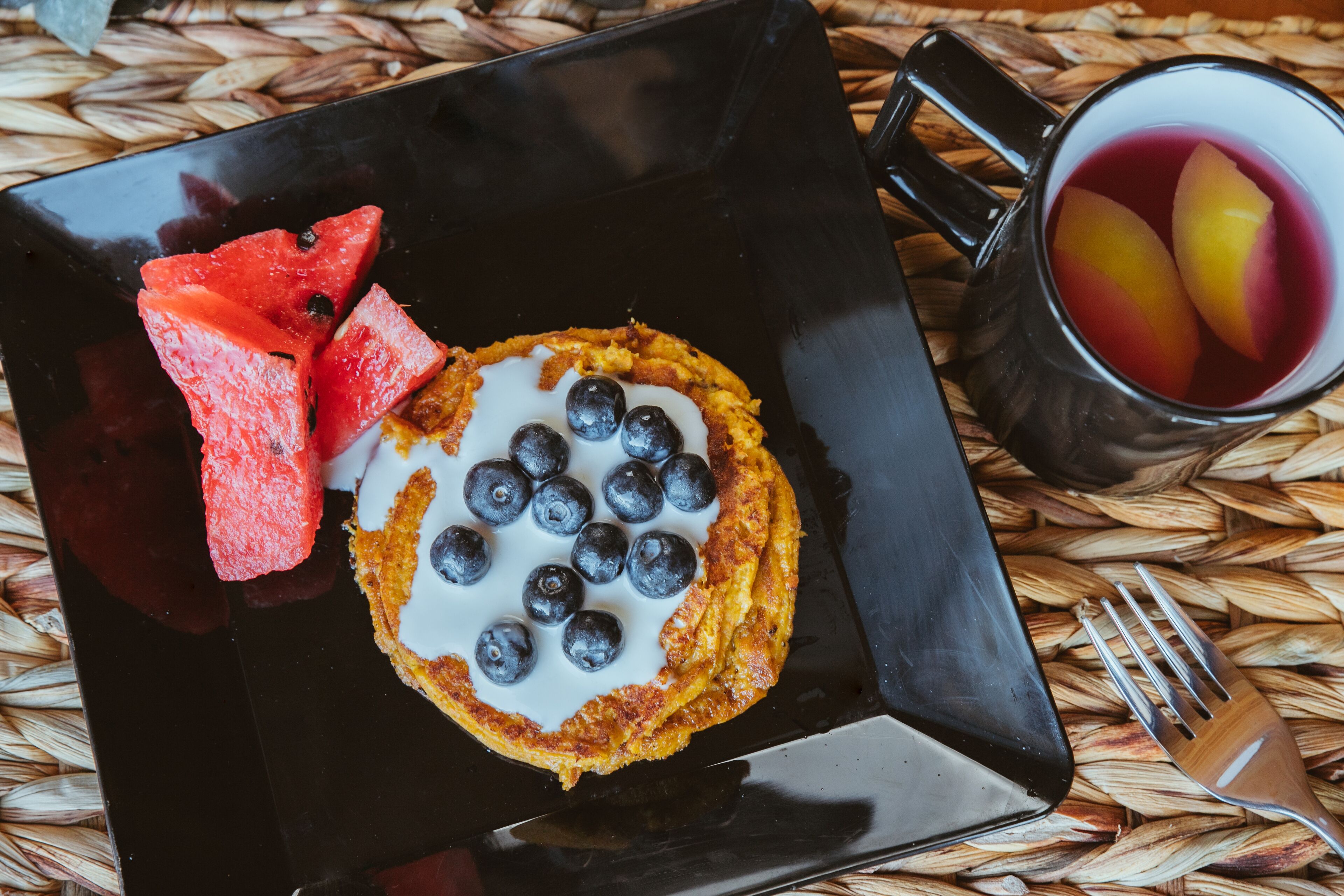 Ein schwarzes, quadratisches Tablett mit einem Blaubeergebäck, einer Wassermelone und einer Tasse mit Fruchtstücken.