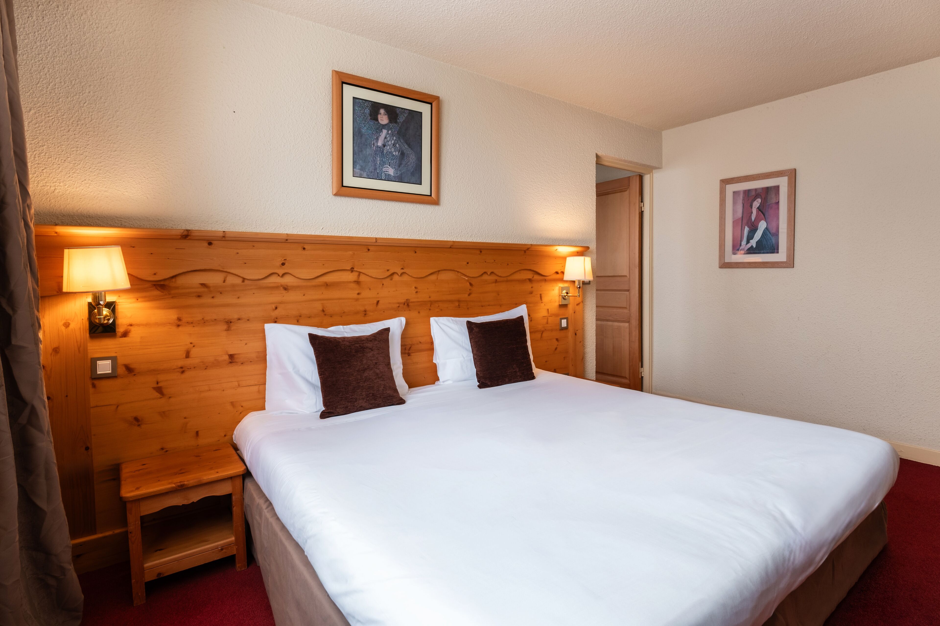 A neatly made bed with white and brown pillows, a wooden headboard, and two wall-mounted lamps.