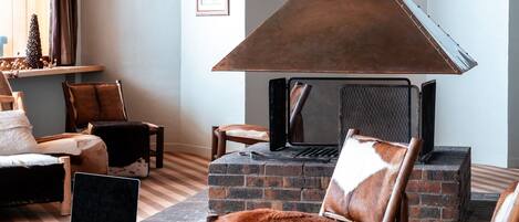A cozy living room with a fireplace, leather furniture, and a laptop on an ottoman.