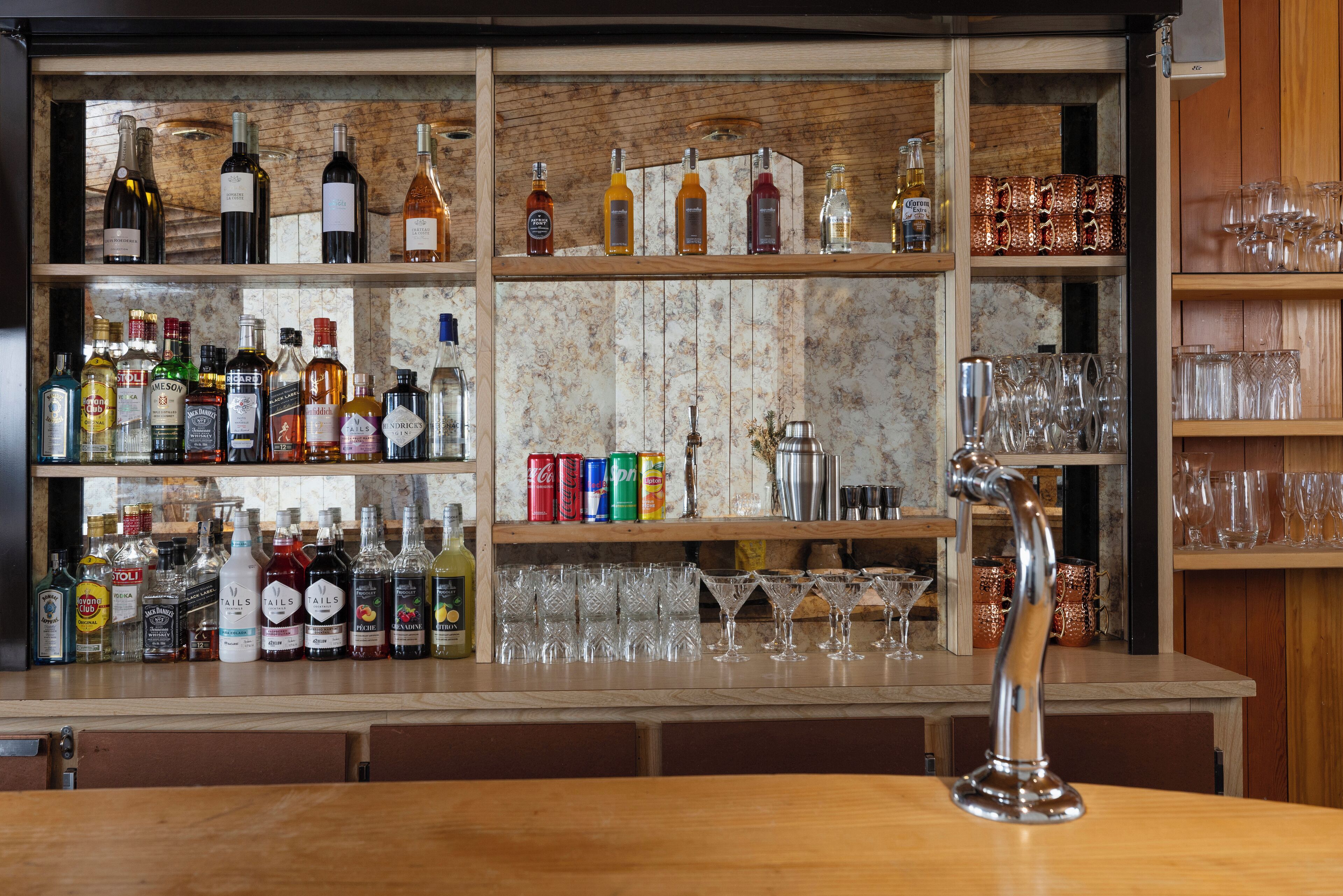 Un espace bar avec des étagères remplies de différentes bouteilles d’alcool, de verres et un robinet de bar.