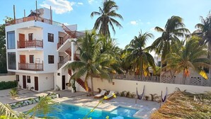 A modern two-story building with a swimming pool, surrounded by palm trees and a thatched-roof structure. - Mexhe Hotel Boutique (El Cuyo)