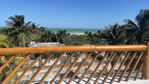 A balcony with a wooden railing overlooking a beach with palm trees and the ocean. - Mexhe Hotel Boutique (El Cuyo)