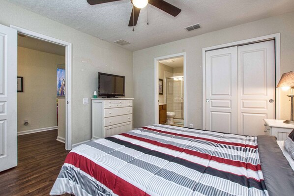 A bedroom with a bed, a television on a dresser, and a ceiling fan.