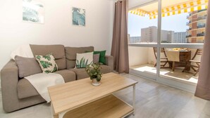 Uma sala de estar moderna com um sofá, mesa de centro e vista da cidade por grandes janelas.