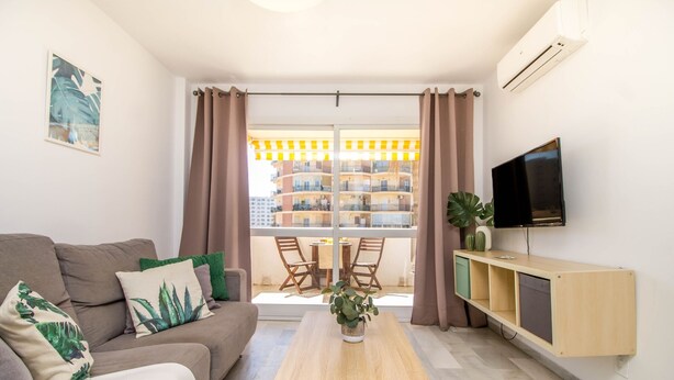 Sala de estar moderna com sofá, mesa de centro, televisão e varanda com vista para um edifício.