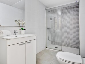 A modern bathroom with a glass-enclosed shower, a white sink with a plant, and a toilet.