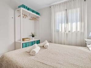 A bedroom with a bed, a wardrobe, a plant, and a window with curtains.