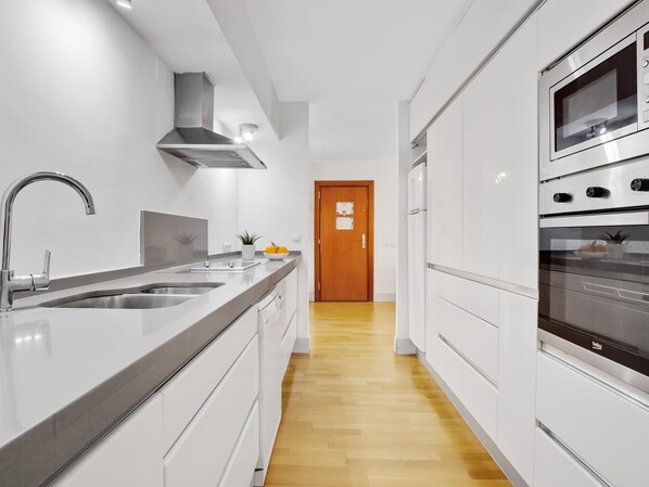 A modern kitchen with a stainless steel sink, a built-in oven, and white cabinetry.