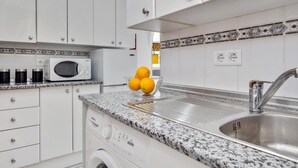 A modern kitchen with white cabinets, a granite countertop, a built-in microwave, a sink, and a washing machine. - Sol Montemar 10 - Terrace, Swimming Pool, Parking, 2 bedrooms (Torremolinos)