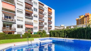 A swimming pool with a clear blue water surface, surrounded by a well-maintained hedge and a multi-story residential building with balconies. - Sol Montemar 10 - Terrace, Swimming Pool, Parking, 2 bedrooms (Torremolinos)