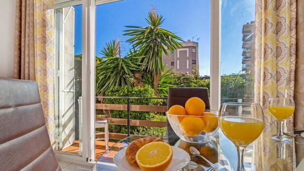 A balcony with a glass table set for breakfast, including a croissant, orange, and a glass of orange juice. - Sol Montemar 10 - Terrace, Swimming Pool, Parking, 2 bedrooms (Torremolinos)