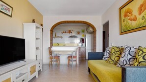 A living room with a TV, a sofa, and a dining area with chairs and a table. - Santa Amalia 51 - Terrace, Swimming Pool, Parking, Sea Views (Torremolinos)