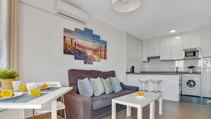 Ein modernes Wohnzimmer mit Sofa, Couchtisch und Essbereich. Man sieht eine Küche mit Geräten und einer Waschmaschine.