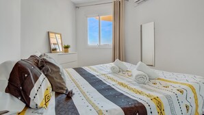 Ein Hotelzimmer mit Bett, einem fenster mit Vorhängen, einer Klimaanlage und einer kleinen Pflanze auf einem Regal.