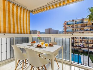 Un balcon avec une table préparée pour le petit-déjeuner, comprenant des croissants, du jus d’orange et un saladier de fruits.
