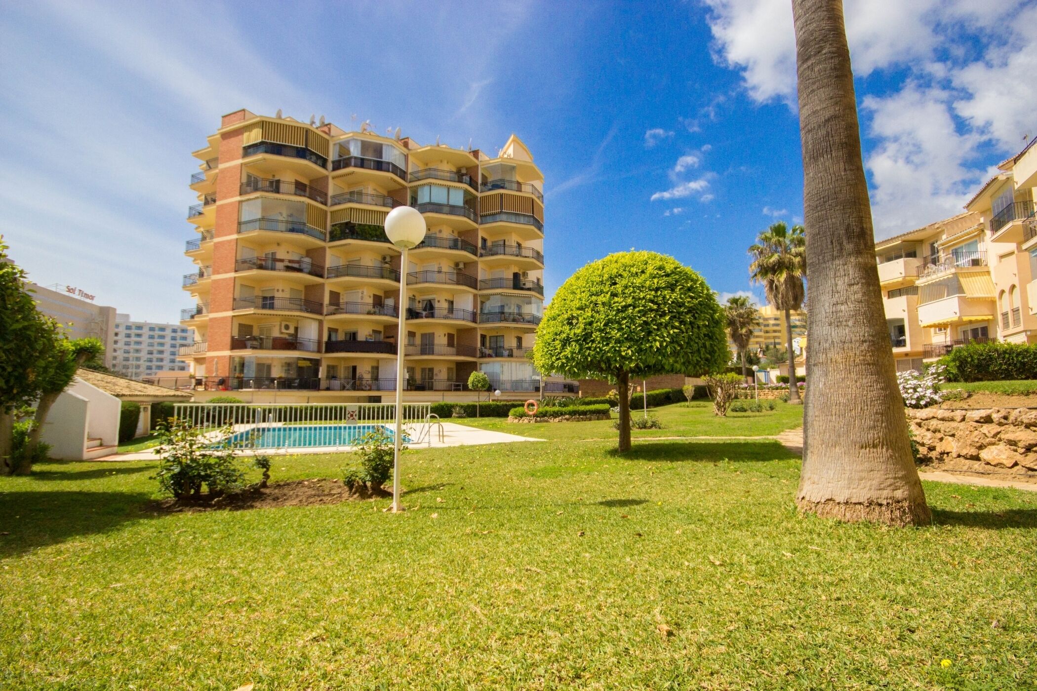 A multi-story residential building with balconies, a swimming pool, and a well-maintained lawn.