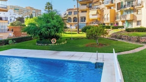 Una piscina con jardín alrededor, un flotador salvavidas y un edificio con balcones.