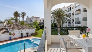 Ein Balkon mit Pool, weiße Gebäude und Palmen im Hintergrund.