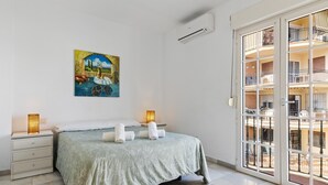 Ein Schlafzimmer mit einem Bett, einem Nachttisch, einem Gemälde und einem Balkon mit Geländer.