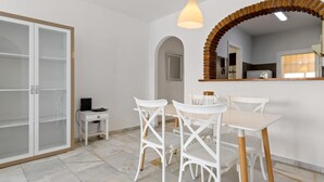 Eine moderne Küche mit weißen Schränken, einem spiegelnden Bogen aus Holz und einem Essbereich mit weißen Stühlen und einem Tisch.