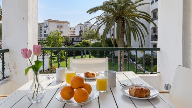 Ein Balkon mit Frühstückstisch, mit Orangen, Saft und einem Croissant.