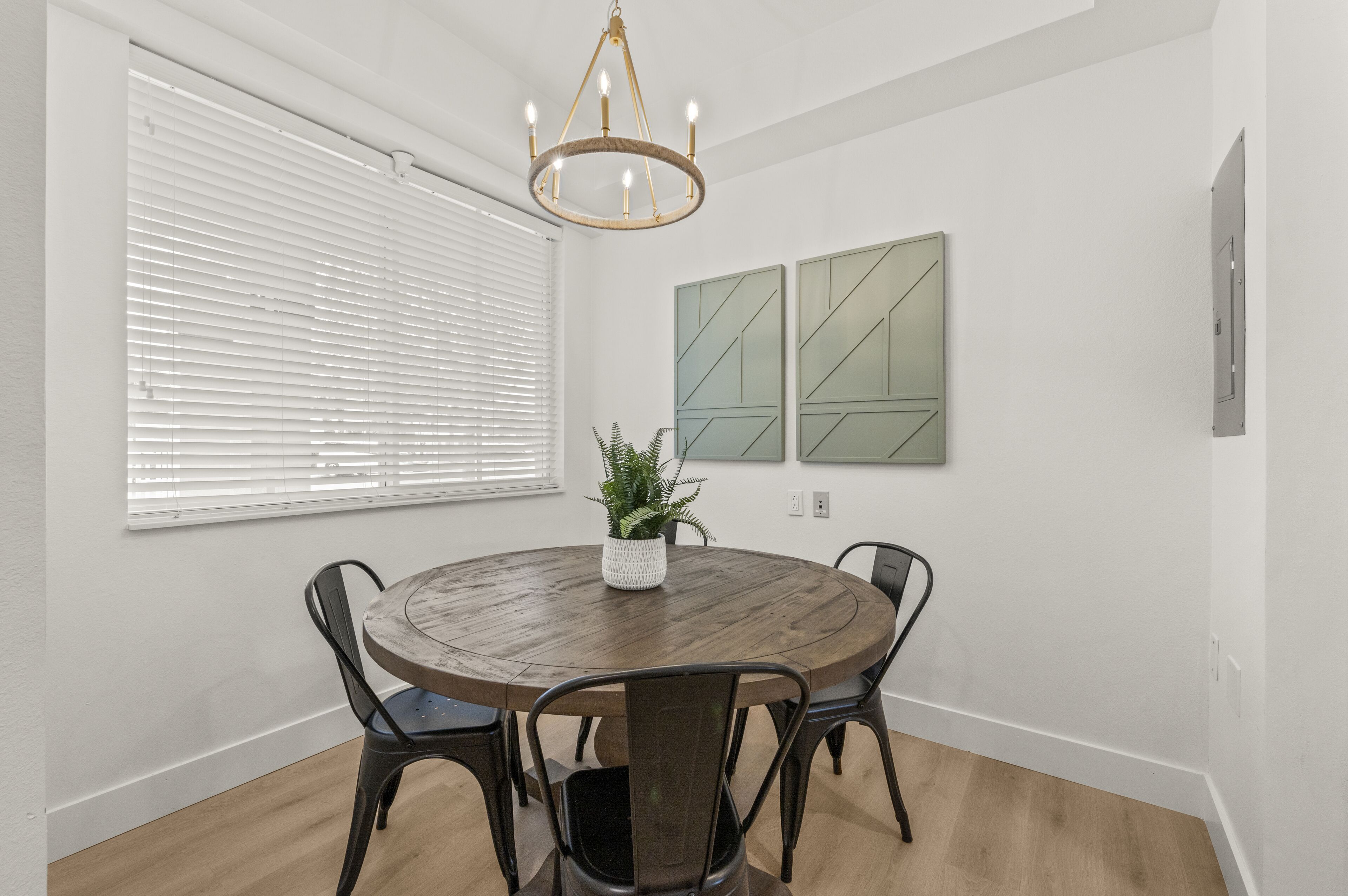 A dining area with a round table, four chairs, a potted plant, and two abstract wall art pieces.