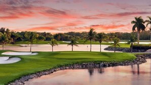 Um campo de golfe com bunkers de areia, lagoas d'água e palmeiras.