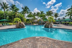 Ein Pool mit Backstein-Terrasse, umgeben von Palmen und Liegestühlen.