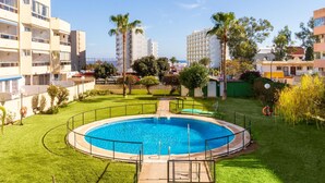 Una piscina rodeada de un césped cuidado, con edificios residenciales al fondo.