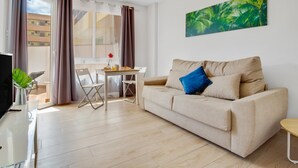 Una sala moderna con un sofá beige, una mesa de comedor y un televisor sobre un mueble.
