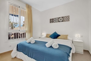Habitación de hotel con una cama, dos mesitas de noche, una ventana con cortinas y una pared con azulejos decorativos.