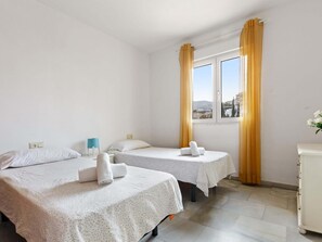 Une chambre d’hôtel avec deux lits, une fenêtre avec des rideaux, une petite table et un placard.