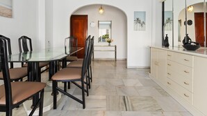 Un coin repas avec une table et des chaises en verre, une porte en bois, un miroir et un sol carrelé.
