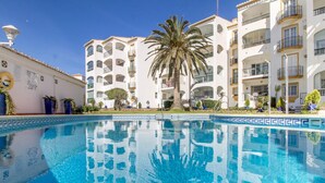 Une piscine à l’eau d’un bleu cristallin, entourée de bâtiments blancs dotés de balcons et de palmiers.