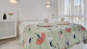 Moderni makuuhuone, jossa on sänky, yöpöydät, seinälle asennettu ilmastointilaite ja läpikuultavat verhot.
