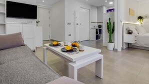 A modern living room with a white sofa, a coffee table with breakfast items, a flat-screen TV, and a minimalist design. - Tropico - Beachfront, 1 bedroom, Carihuela (Torremolinos)