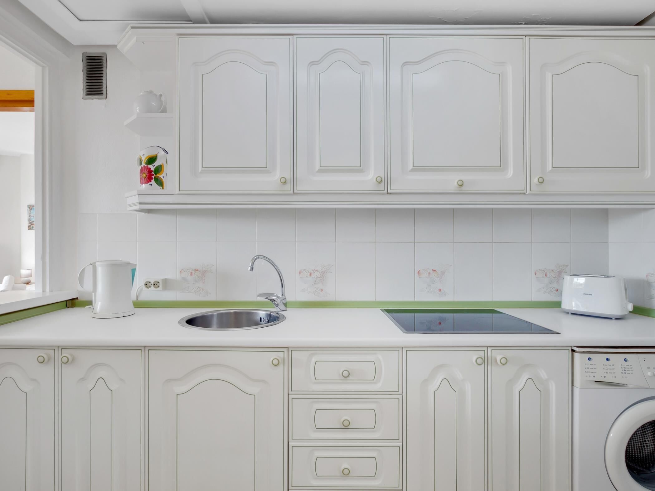 A kitchen with white cabinets, a sink, a toaster, and a washing machine.