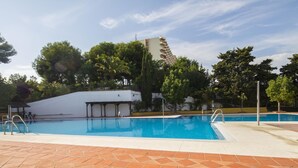 A swimming pool with tiled deck, surrounded by trees and a white building with balconies.