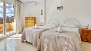 A hotel room with two beds, a wooden dresser, a painting, and a view of the city.