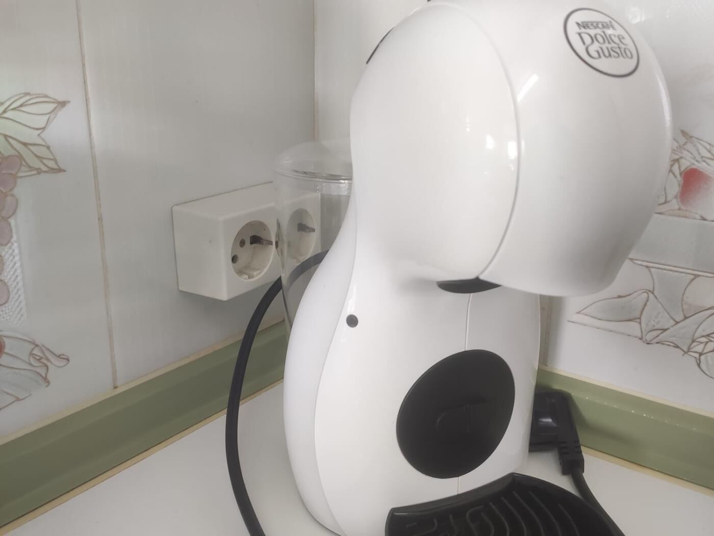 A white hair dryer with a black handle and a cord plugged into a wall socket.
