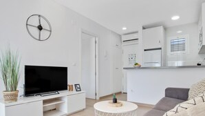 En moderne stue med et fladskærms-tv, et hvidt tv-møbel, en grå sofa og et lille rundt sofabord.