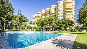 A swimming pool surrounded by a well-maintained lawn, with a multi-story building in the background.