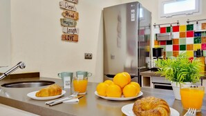 A kitchen with a stainless steel refrigerator, a sink, and a breakfast setup including croissants and oranges.
