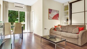 A modern living room with a glass coffee table, a beige sofa with red cushions, and a dining area with a glass table and chairs.