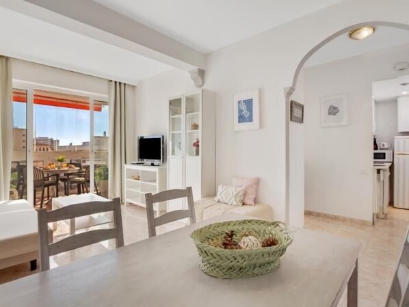 A modern living room with a dining area, a TV, and a balcony with a city view.