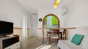 A hotel room with a TV, a dining table with chairs, a sofa, and a kitchen visible through an archway. - Vistamarina 405B - Terrace, Swimming Pool, 300m from beach (Torremolinos)