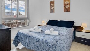 A bedroom with a bed, bedside tables, a desk, and a window with a view of buildings and sky. - Vistamarina 405B - Terrace, Swimming Pool, 300m from beach (Torremolinos)