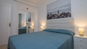 A bedroom with a bed, bedside lamps, a mirror, and a painting on the wall. - Imperial Puerto 3E - Terrace, Swimming Pool, 200m from the beach (Torremolinos)